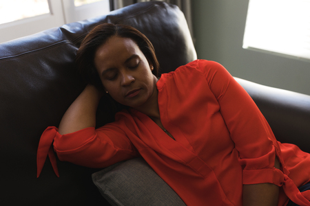 Front view of a senior woman sleeping on the sofa in living room at homeの写真素材