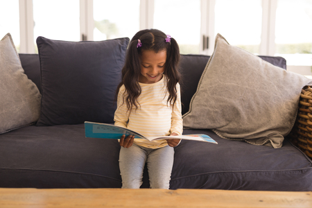 Front view of an African American girl reading a story book in living room at homeの写真素材