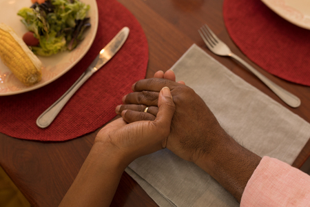 Close-up of  African American father and daughter holding each other hand and praying before having meal on dining table at homeの写真素材