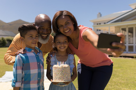 Front view of an African American multi-generation family taking selfie with mobile phone while...