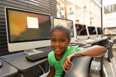 Front view of a happy African American schoolgirl sitting in the library at schoolの写真素材
