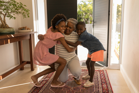 Front view of a happy African American grandmother embracing her grandchildren while sitting on her knees at homeの写真素材