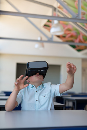 Front view of a Caucasian schoolboy using virtual reality headset at desk in a classroom at school