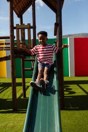 Front view of a cute African American schoolboy playing on a slide at school playground on a sunny dayの写真素材