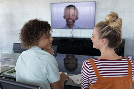 Rear view of young multi-ethnic business colleagues interacting with each other in a conference room...