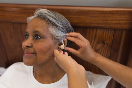 Close-up of African American female doctor fitting senior African American woman with hearing aid at...