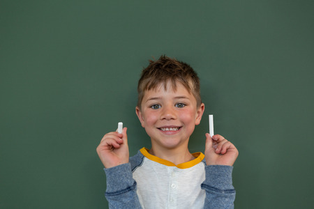Front view of Caucasian schoolboy holding chalk against chalkboard in a classroom at elementary schoolの写真素材