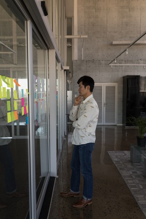 Side view of standing young Asian male executive looking at chart in modern office