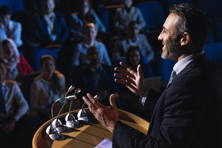 Side view of Caucasian businessman standing and giving presentation in the auditoriumの写真素材
