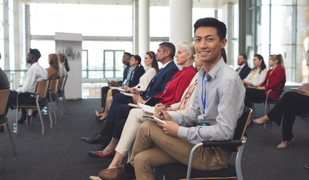 Side view of happy Asian businessman looking at camera at a business seminar in office buildingの写真素材