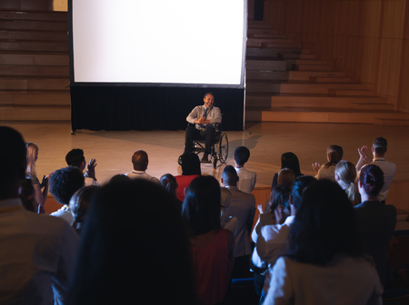 High view of Caucasian businessman sitting on a wheelchair and giving presentation to the audience in the auditoriumの写真素材