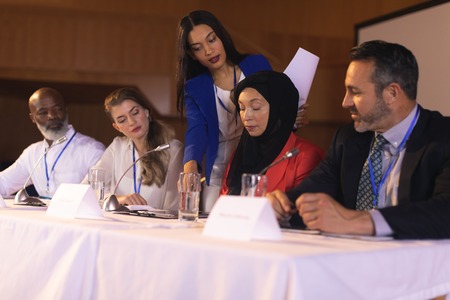 Front view of young mixed race businesswoman showing documents to the panel of speaker