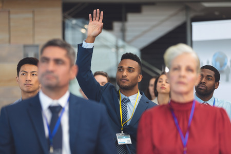 Front view of young mixed race businessman raising hand in a business seminar in office buildingの写真素材