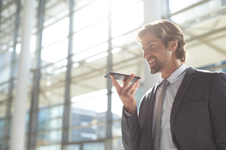 Low angle view of happy young Caucasian businessman talking on mobile phone in lobby officeの写真素材