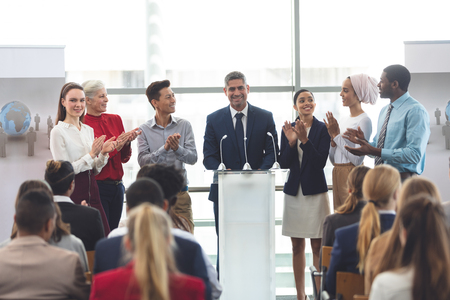 Front view of diverse business professionals standing on podium while speaking at a business seminar in office buildingの写真素材