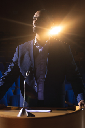 Front view of handsome mixed race businessman standing on stage in auditorium. Businessman thinkingの写真素材