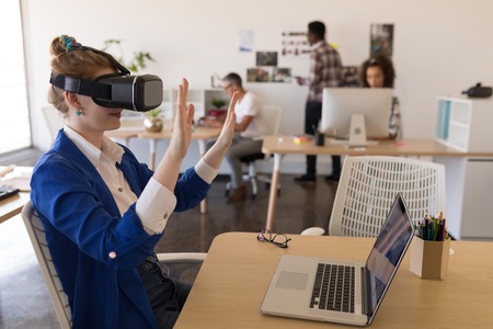 Side view of young Caucasian businesswoman using virtual reality headset at desk in modern office