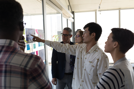 Side view of standing mixed race business colleagues discussing over chart in modern officeの写真素材