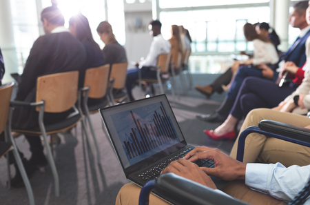 Mid section of disabled young African american businessman using laptop during seminar in office buildingの写真素材