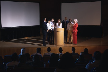 Front view of mixed race business colleague standing and  discussing with each other in the auditorium stage in front of the audienceの写真素材