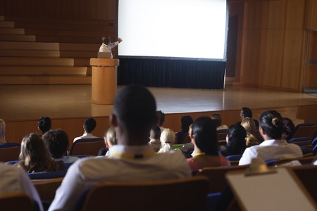 Front view of old African-American businessman standing around podium and giving presentation in the auditoriumの写真素材