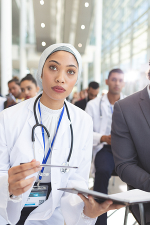 Front view of mixed race  female doctor with notebook and pen attending seminar in conference roomの写真素材