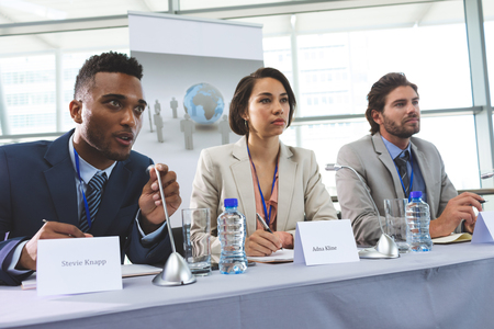 Front view of young mixed race business people sitting at table in seminar
