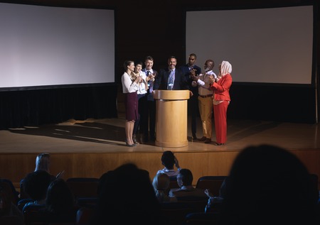 Front view of mixed race business colleagues clapping hand for there colleague  for the success in the auditorium stage in front of the audienceの写真素材