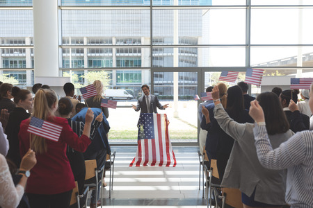 Front view of american businessman speaking at a business seminar in office building with american flagsの写真素材