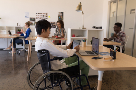 Side view of young disabled Asian male executive using digital tablet at desk in modern office....