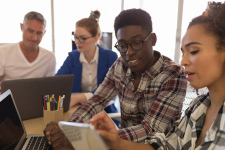 Side view of young African-American male and pretty mixed race female executives discussing over digital tablet in modern officeの写真素材
