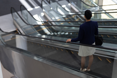 Rear view of pretty young mixed-race businesswoman using escalator in modern officeの写真素材