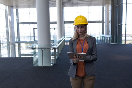 Front view of young blonde Caucasian female architect using digital tablet in modern office