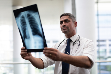 Front view of attentive mature Caucasian male doctor looking at x-ray standing in clinic