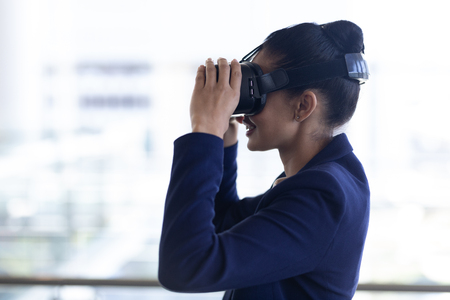 Side view of happy young mixed-race businesswoman using virtual reality headset in modern office