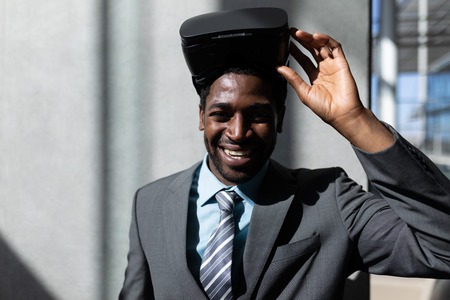Front view of happy African-American businessman with virtual reality headset looking at camera...