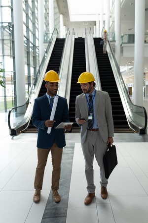 Front view of young multi-ethnic male architect discussing over digital tablet standing in office...