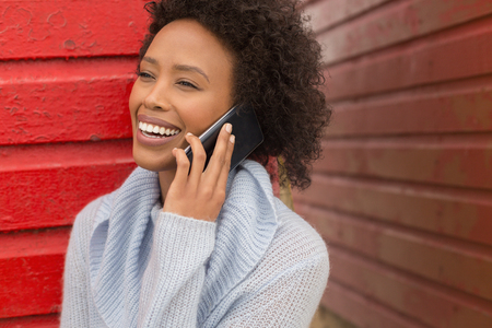 Front view of pretty happy young African American woman talking to her mobile phone at red beach hut. She is smilingの写真素材