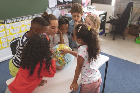 High angle view of a teacher and school kids interacting about a earth globe in classroomの写真素材