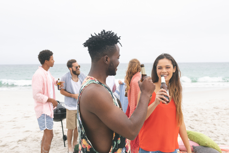 Front view of multi ethnic friends enjoying and interacting on beach while having beerの写真素材