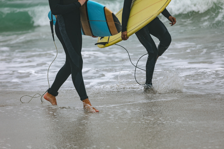 Low section of younf multi-ethnic male friends walking on beach while holding surfboardsの写真素材