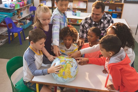 Schoolteacher showing at his school kids the earth globe in classroom at schoolの写真素材
