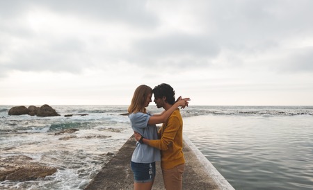 Side view of young Caucasian couple kissing each other standing on rock near beachの写真素材