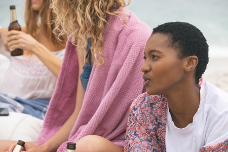 Side view of african american woman lying and interacting with friends on beachの写真素材