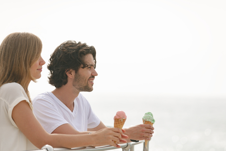 Side view of happy young Caucasian couple standing at promenade while having ice cream cone. They are smilingの写真素材