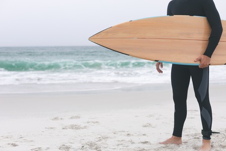 Low section of young male surfer holding surfboard on the beachの写真素材