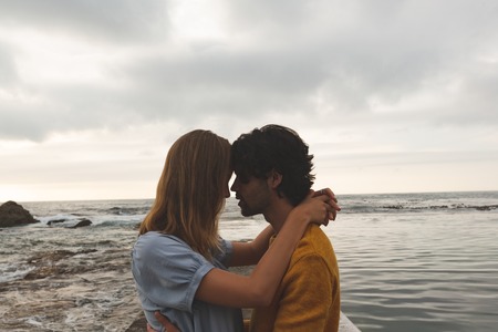 Side view of young Caucasian couple kissing each other standing on rock near beachの写真素材