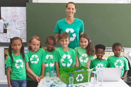 Portrait of caucasian teacher and happy multi ethnic student standing together and looking at camera in classroomの写真素材