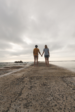 Rear view of Caucasian couple standing hand in hand on the rock near beachの写真素材