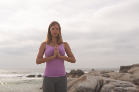 Front view of Caucasian blonde woman perform yoga on the beach on sunny day. She is relaxedの写真素材